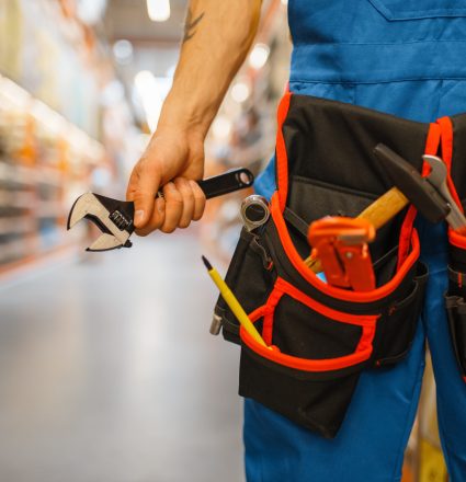 Male builder choosing tool belt at the shelf in hardware store. Constructor in uniform look at the goods in diy shop