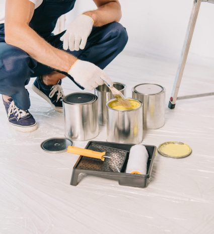 cropped view of painter taking yellow paint from can with paintbrush cropped view of painter taking yellow paint from can with paintbrush