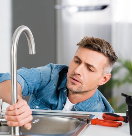 handsome man repairing faucet of kitchen sink handsome man repairing faucet of kitchen sink