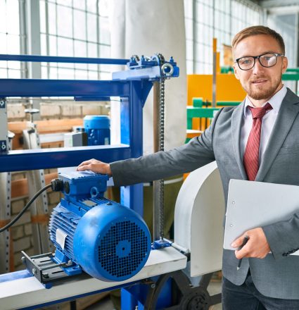 Successful Seller Presenting Work Tools Portrait of successful salesman wearing suit posing looking at camera, standing by machine tools in industrial showroom