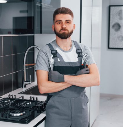 Young professional plumber in grey uniform standing on the kitchen.