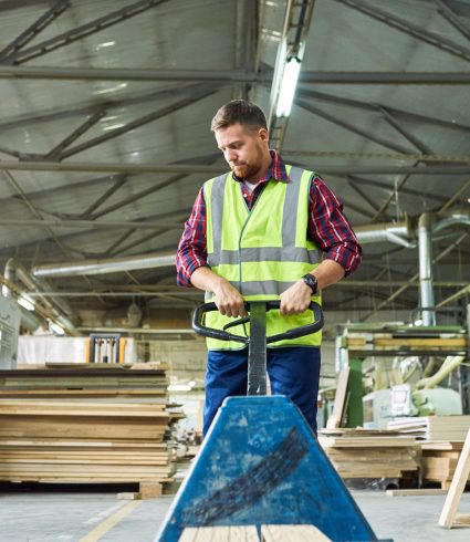 Portrait of young man wearing reflective jacket pulling cart in factory warehouse, copy space